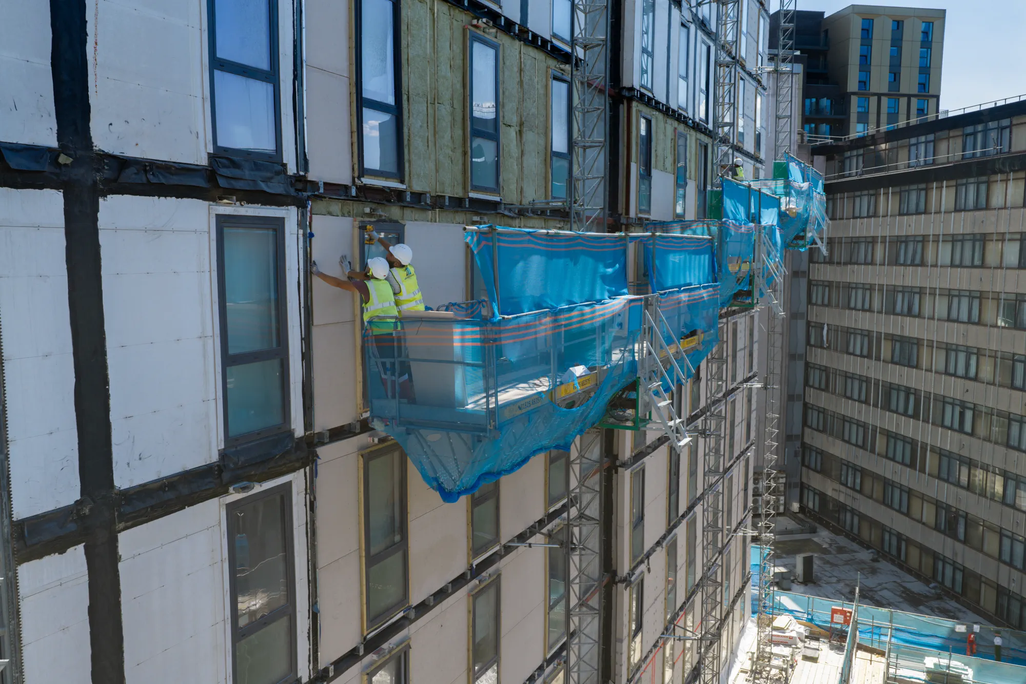 ukr-facades-grand-felda-house-wembley-project-aerial-22 Operatives working on mast climbers from external access platforms during facade construction at Grand Felda House in Wembley